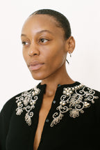 Woman wearing a black top with intricate white embroidery on a white background
