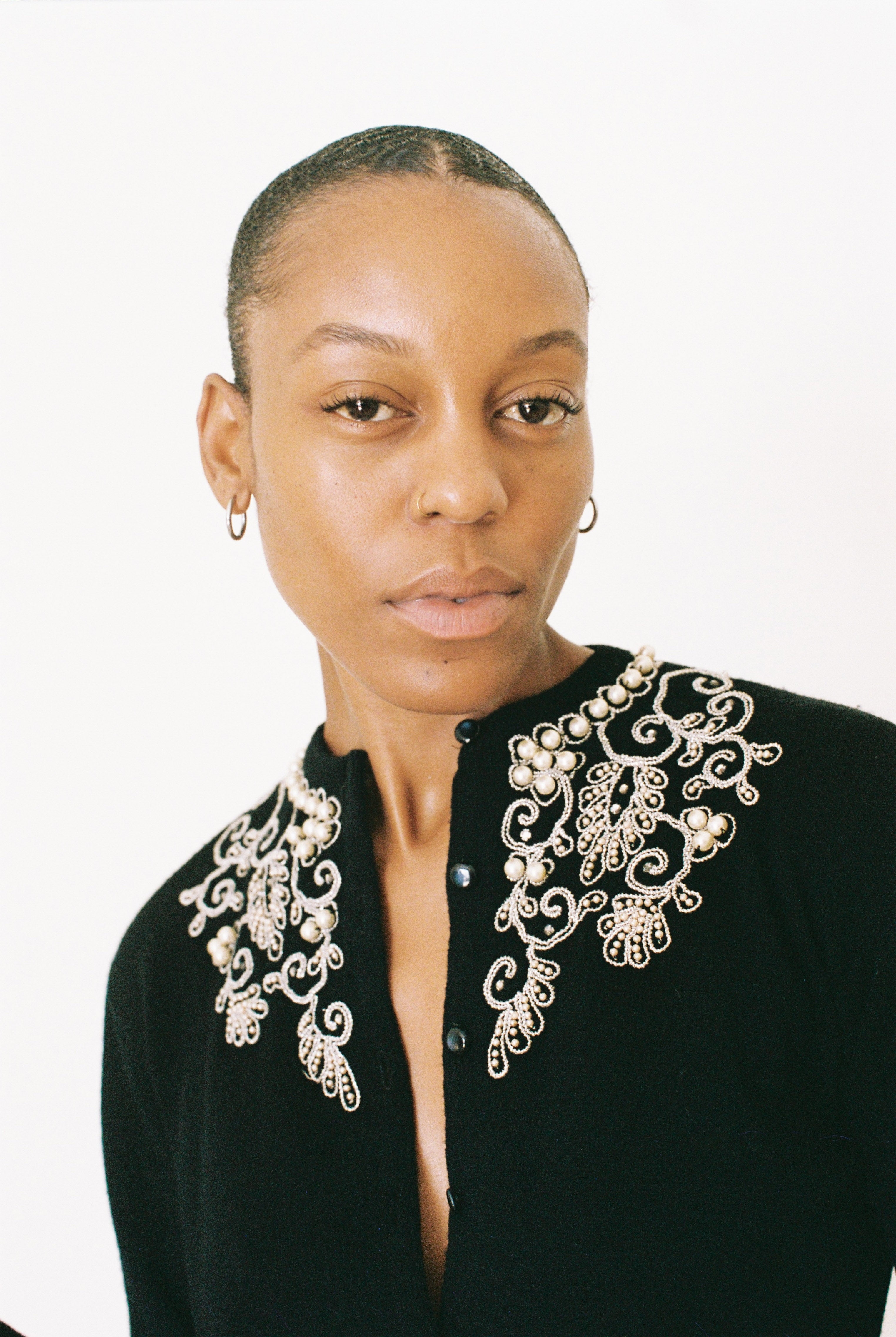 Woman wearing a black top with intricate white embroidery on a white background