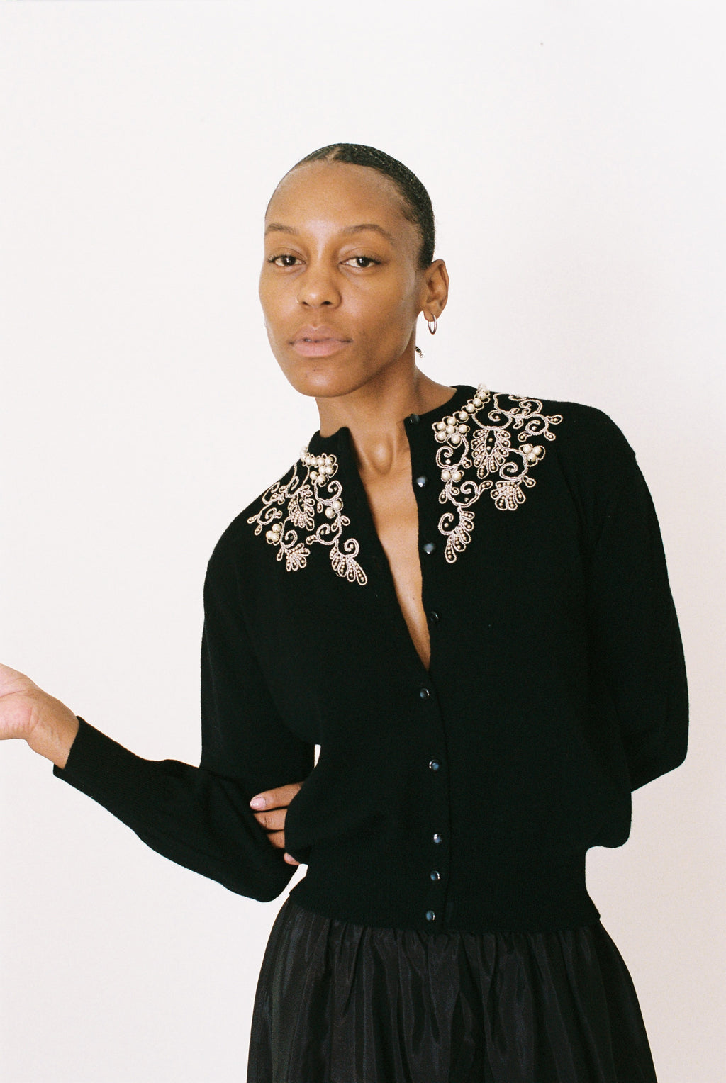 Woman wearing a black cardigan with decorative collar against a white background