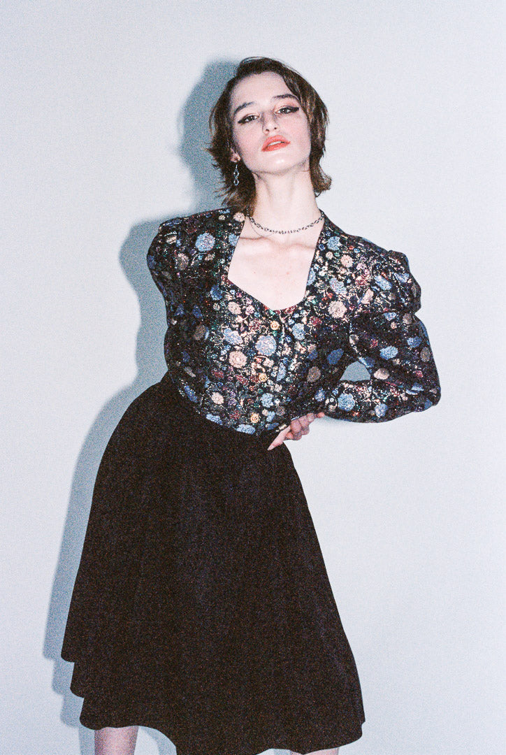 Woman wearing a floral blouse and black skirt against a light background