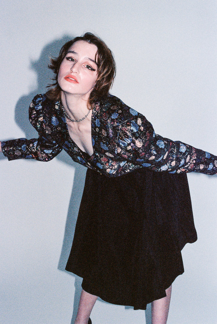 Person wearing a floral blouse and black skirt against a light blue background