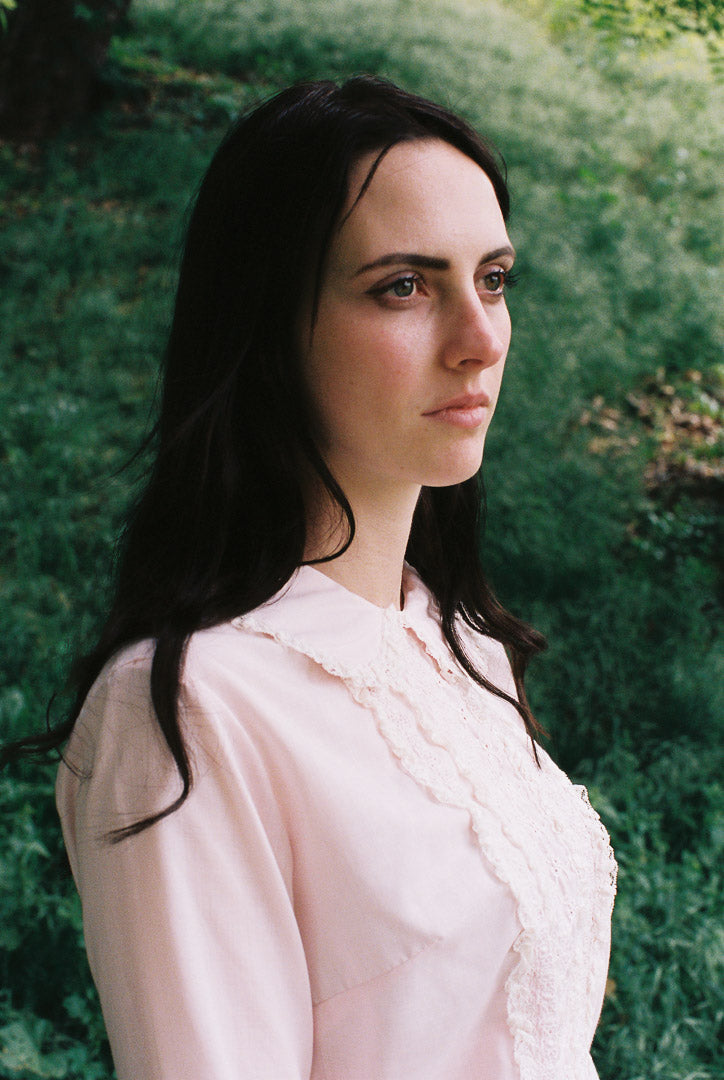 Woman in a light pink blouse standing against a green natural background
