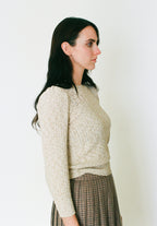 Woman wearing a textured beige sweater against a plain background