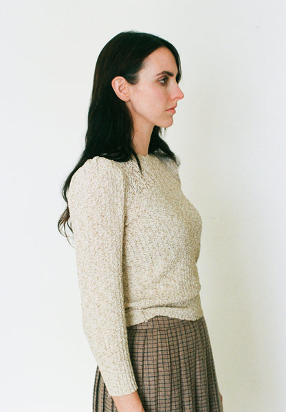 Woman wearing a textured beige sweater against a plain background