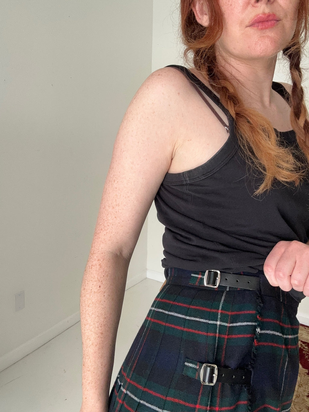 Person wearing a black tank top and plaid skirt indoors.