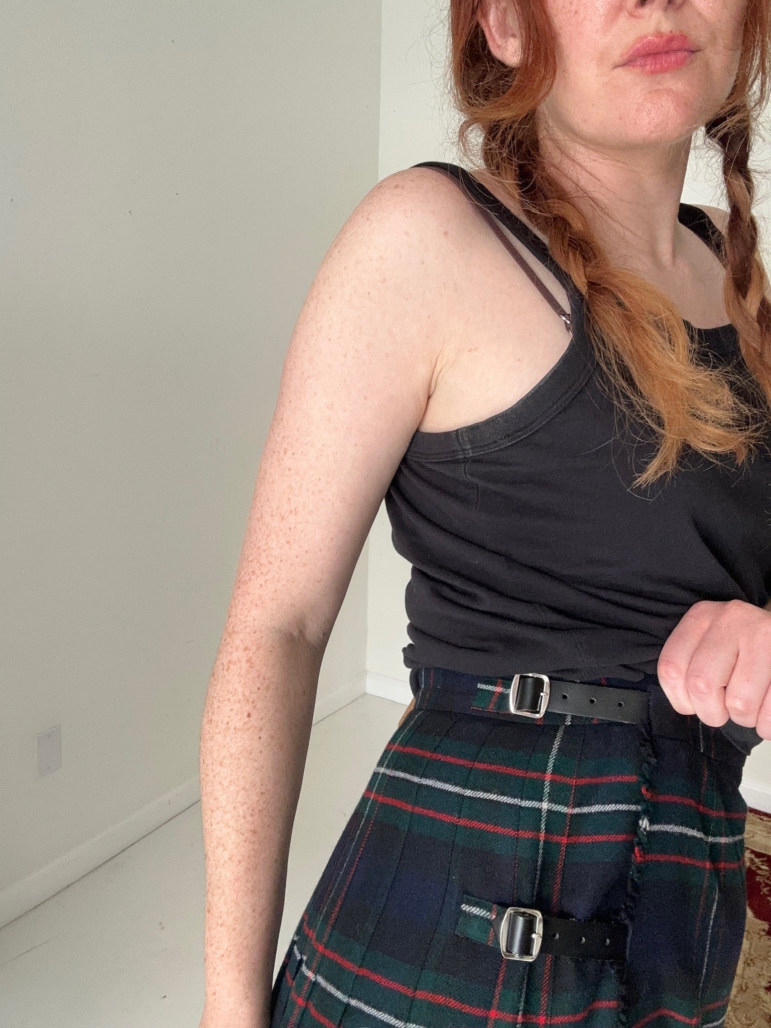 Person wearing a black tank top and plaid skirt indoors.