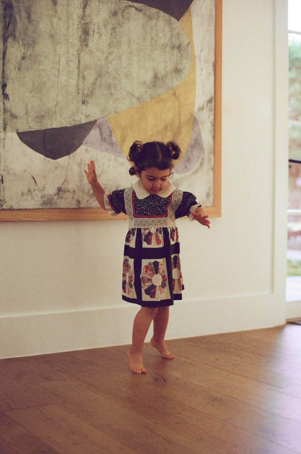 Child in a patterned dress standing in front of a large abstract painting.