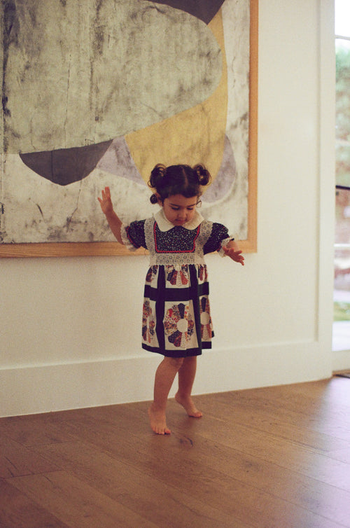 Child in a patterned dress standing in front of a large abstract painting.