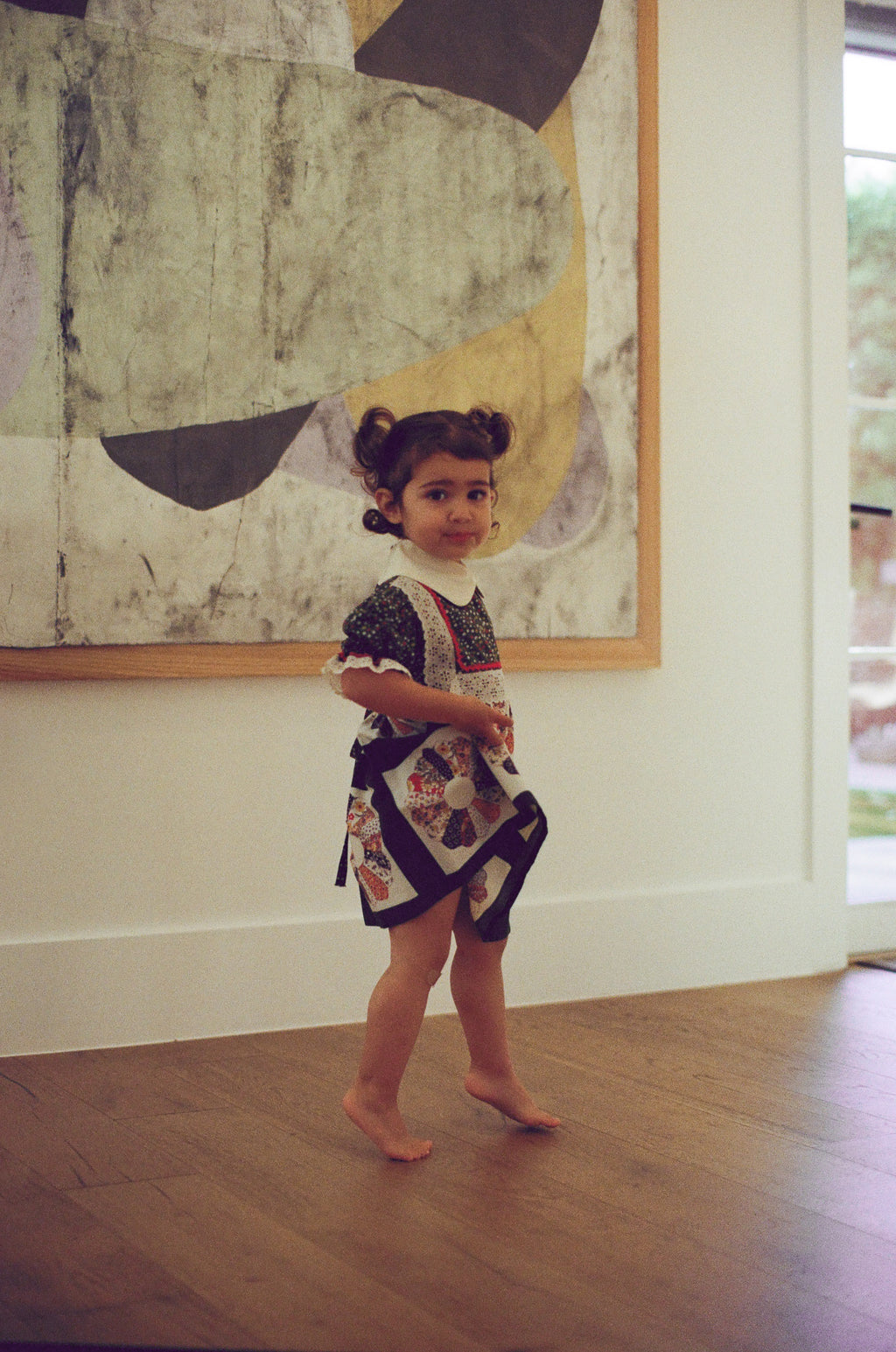 Young girl in a patterned dress standing in front of an abstract painting