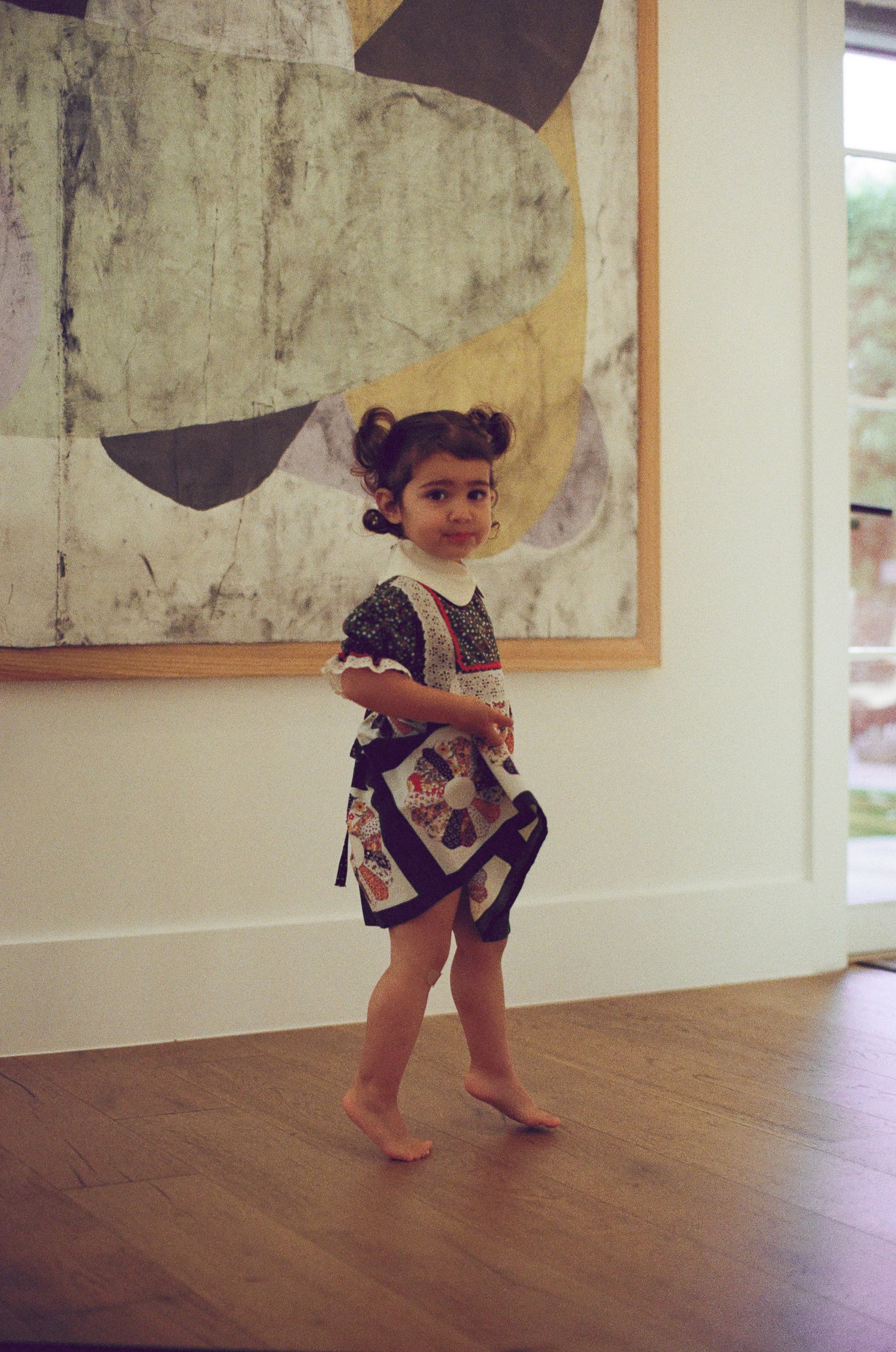 Young girl in a patterned dress standing in front of an abstract painting