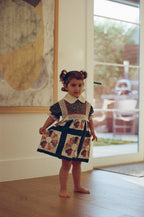 Young girl in a patterned dress standing in a room with a large window.