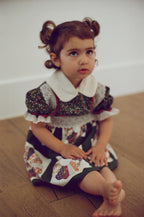 Young girl in a patterned dress sitting on a wooden floor.