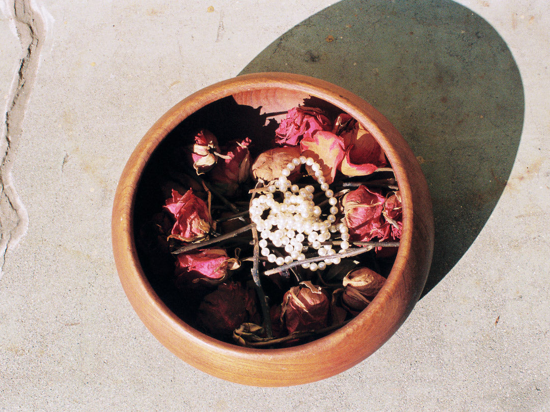 Wooden bowl with dried flowers and a pearl necklace on a light stone surface