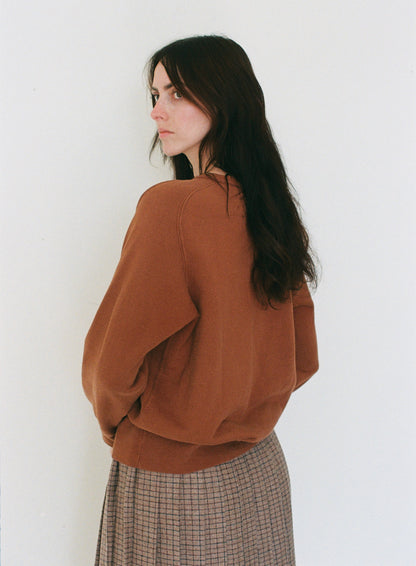 Woman wearing a brown sweater and plaid skirt against a white background