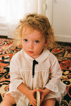 Young girl in a white dress sitting on a patterned rug.