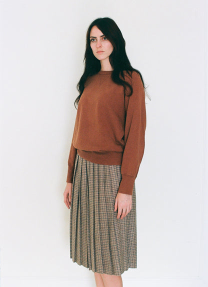 Woman wearing a vintahe brown sweater and vintage plaid skirt on a white background