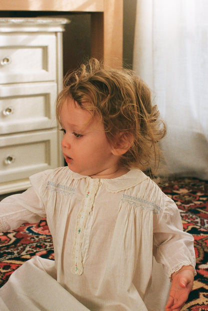 Child in a white dress sitting on a patterned rug with a neutral background