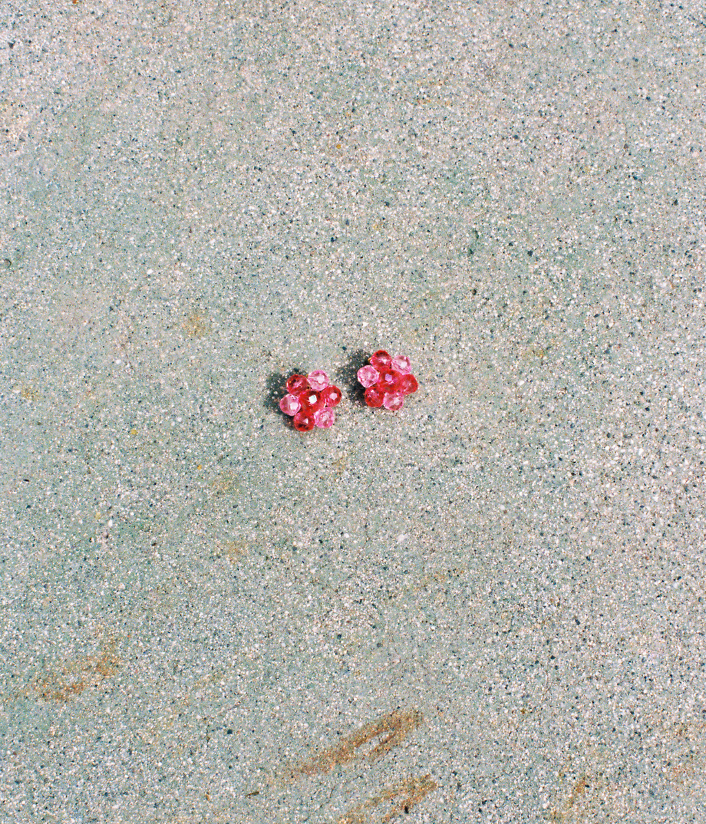Two pink earrings on a textured beige surface
