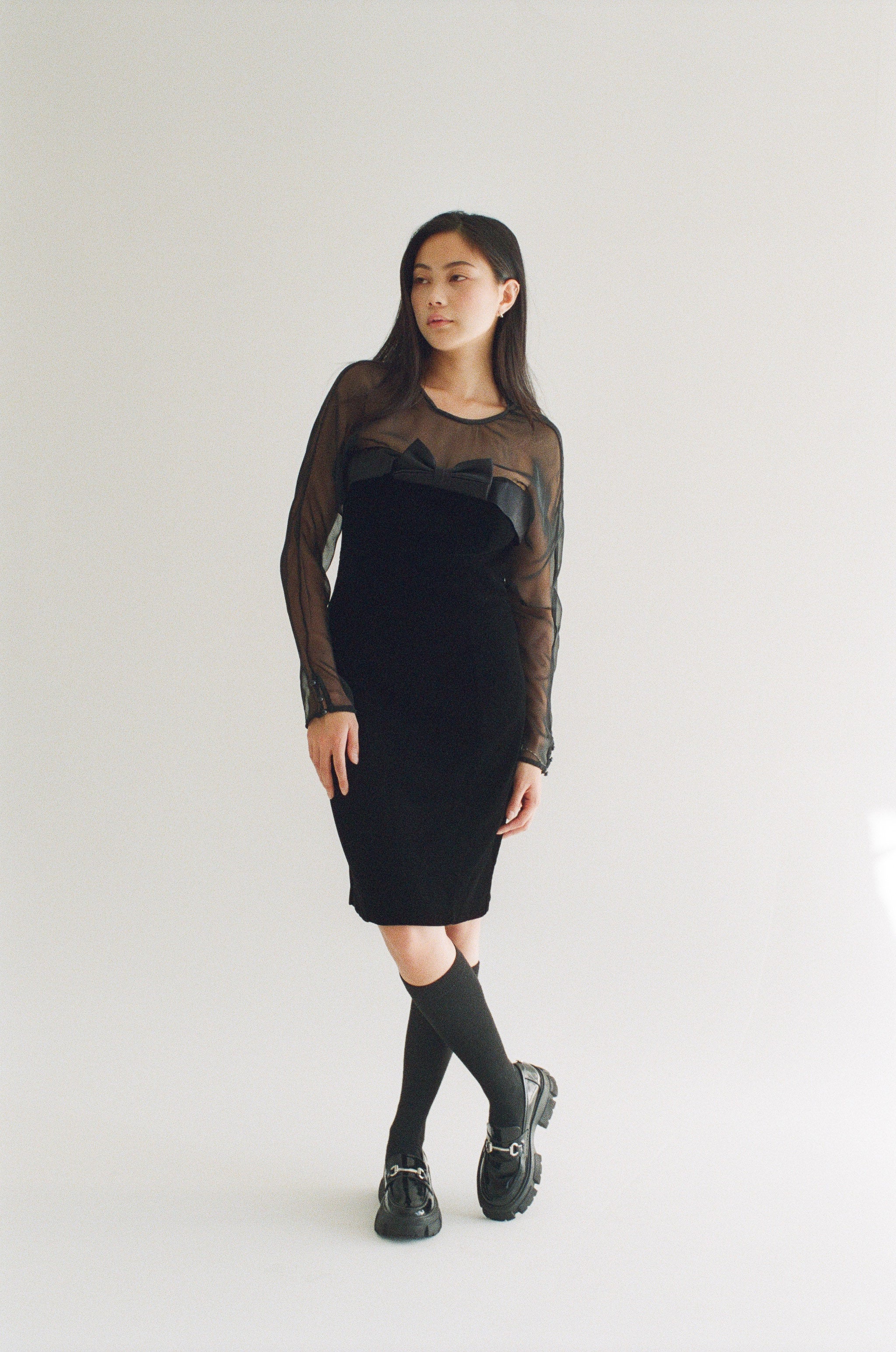 Person wearing a black dress with sheer sleeves on a white background
