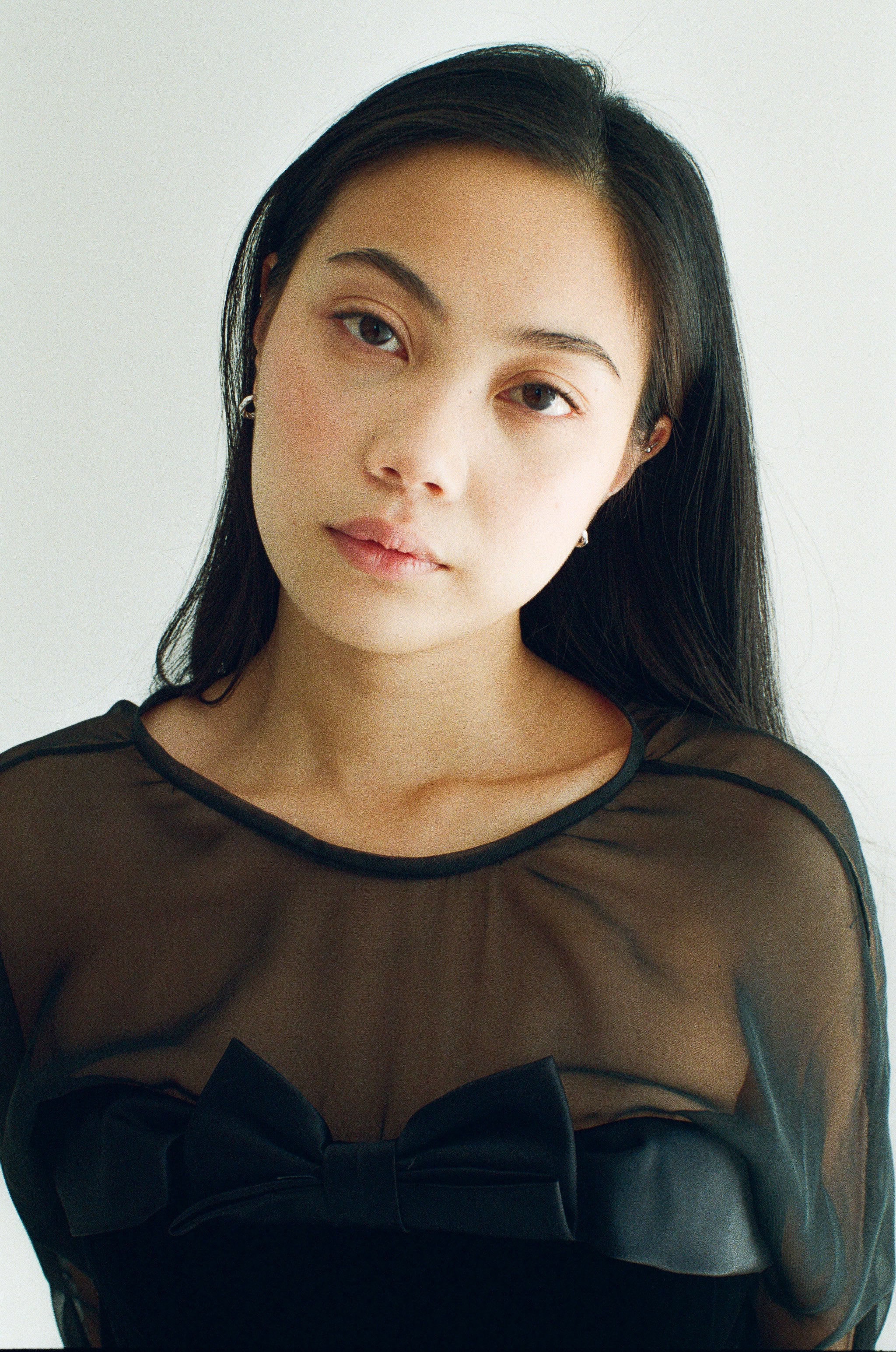 Woman wearing a sheer black dress with a bow detail against a plain background