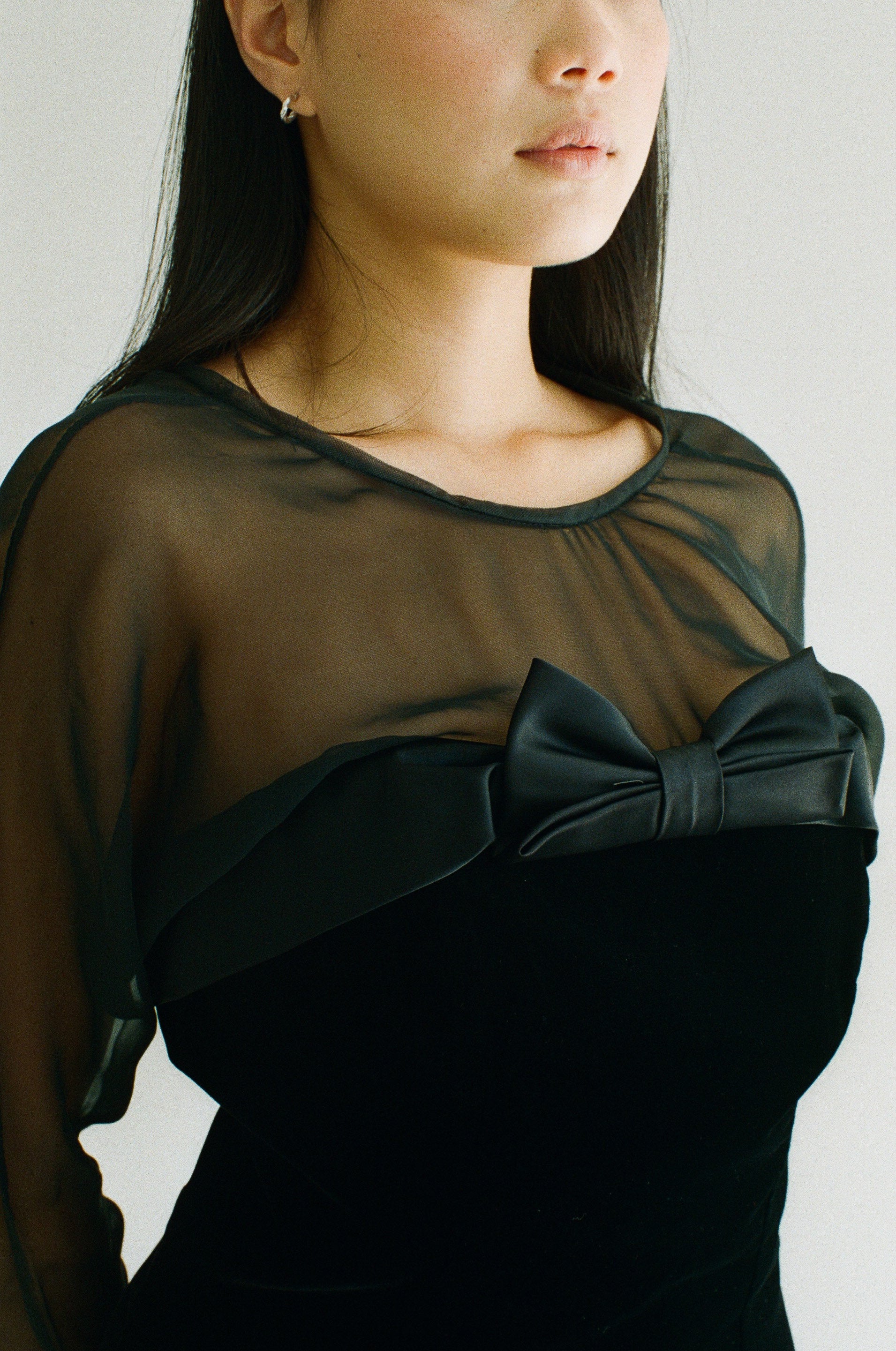 Woman wearing a black dress with a large bow detail on a plain background