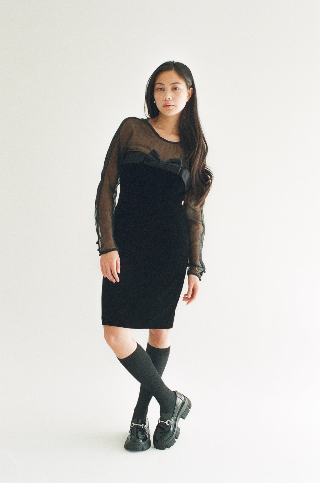 Woman wearing a black dress with sheer sleeves against a white background