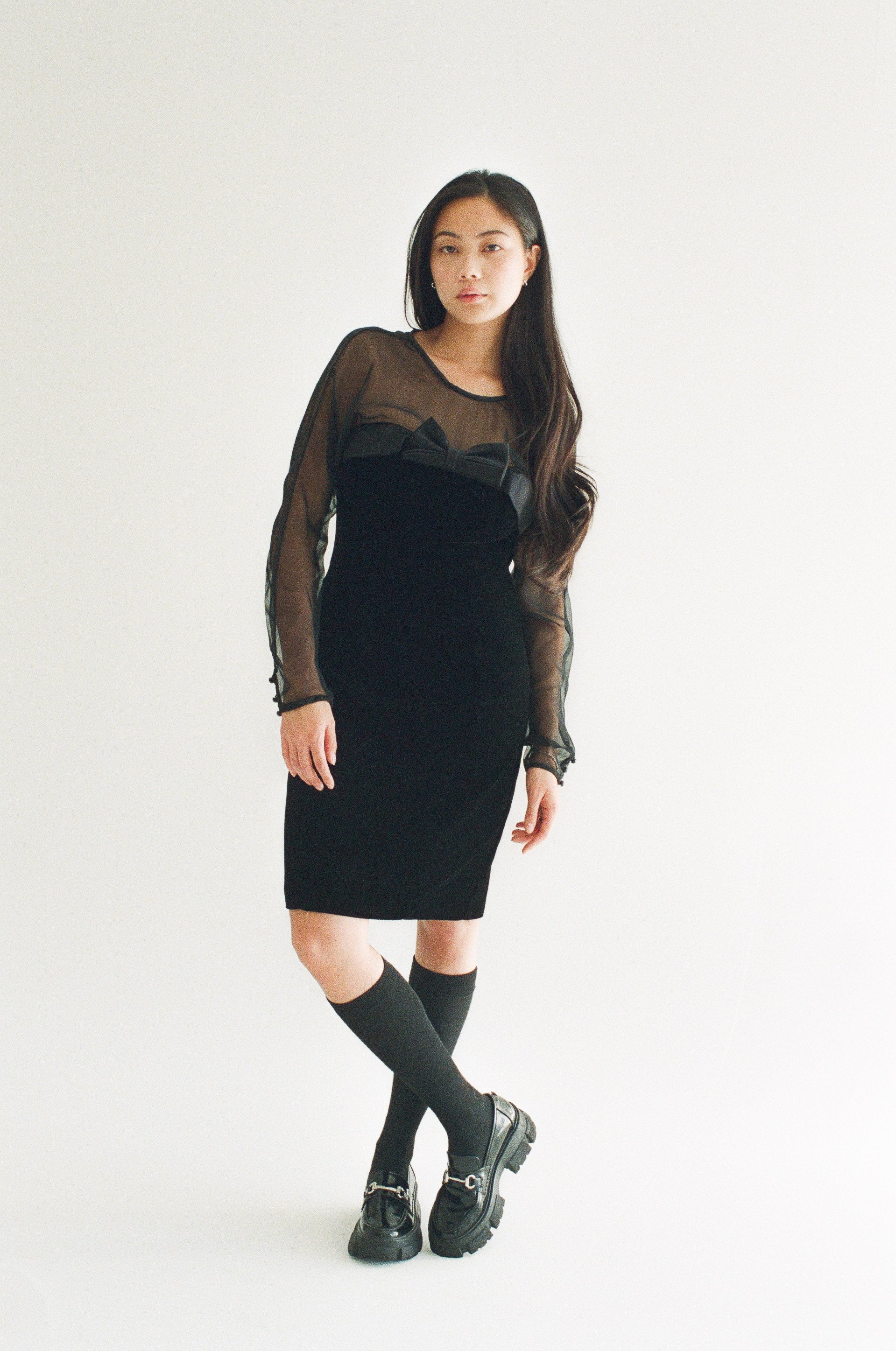 Woman wearing a black dress with sheer sleeves against a white background