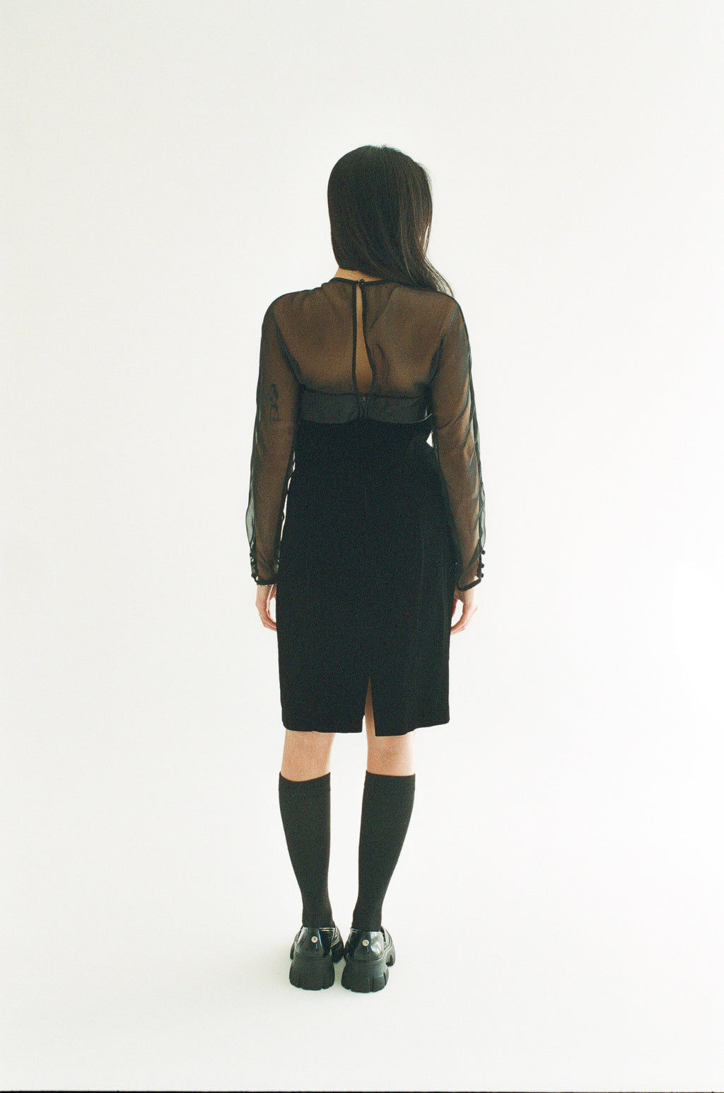 Person wearing a black dress with sheer sleeves on a white background