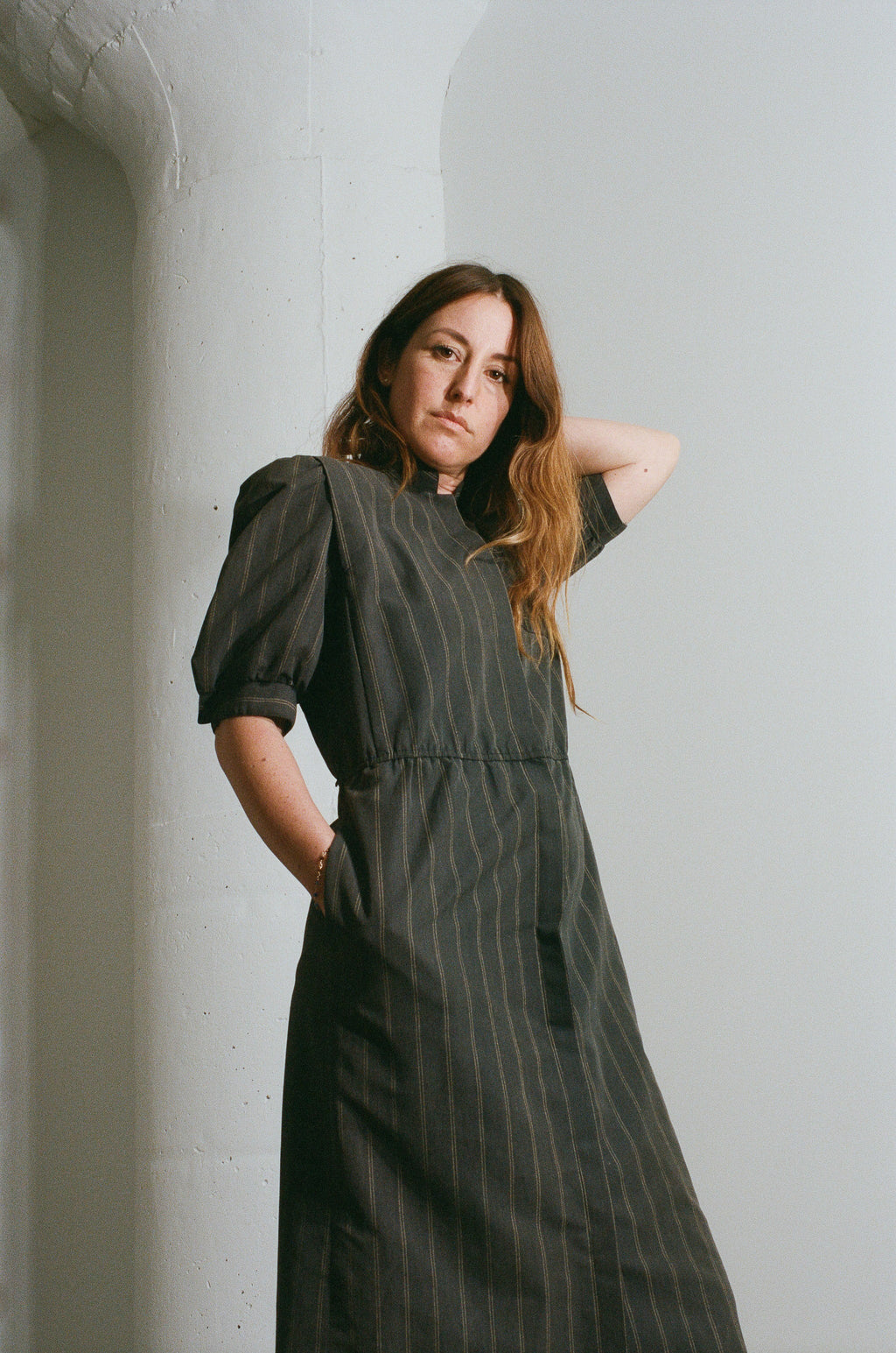 Woman wearing a dark green pinstripe dress against a light gray wall.