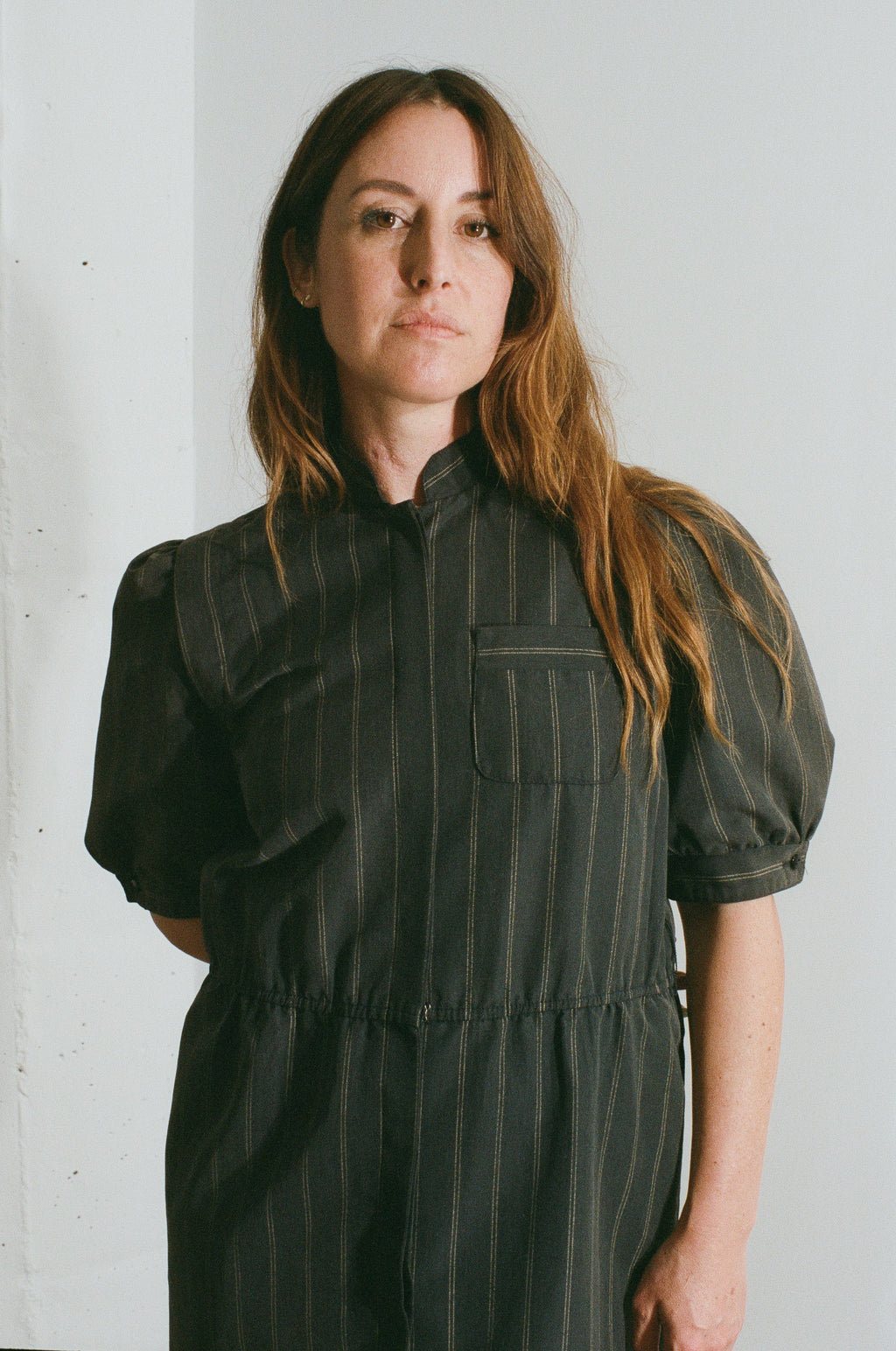 Woman wearing a black pinstripe dress against a white wall