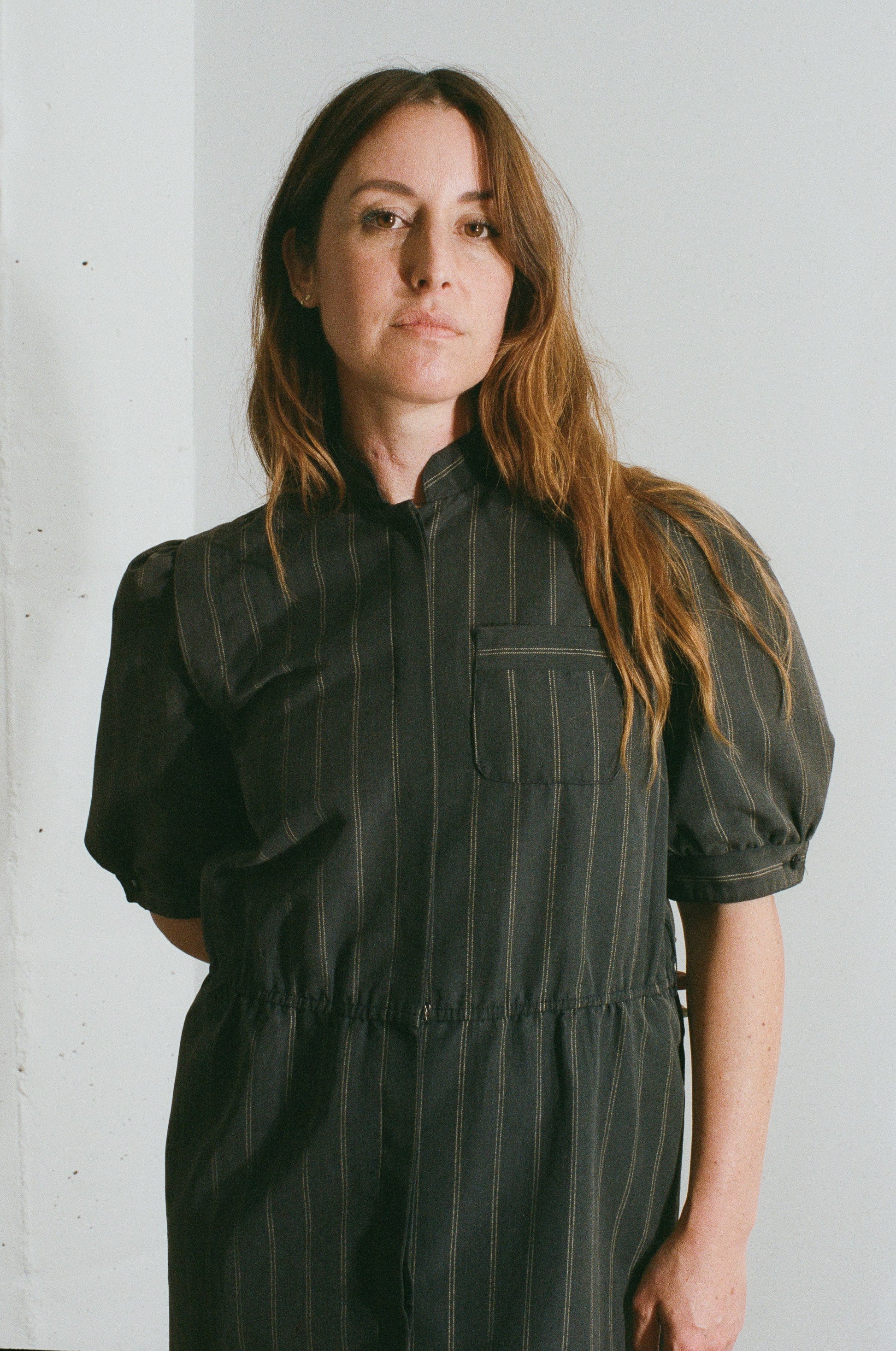Woman wearing a black pinstripe dress against a white wall
