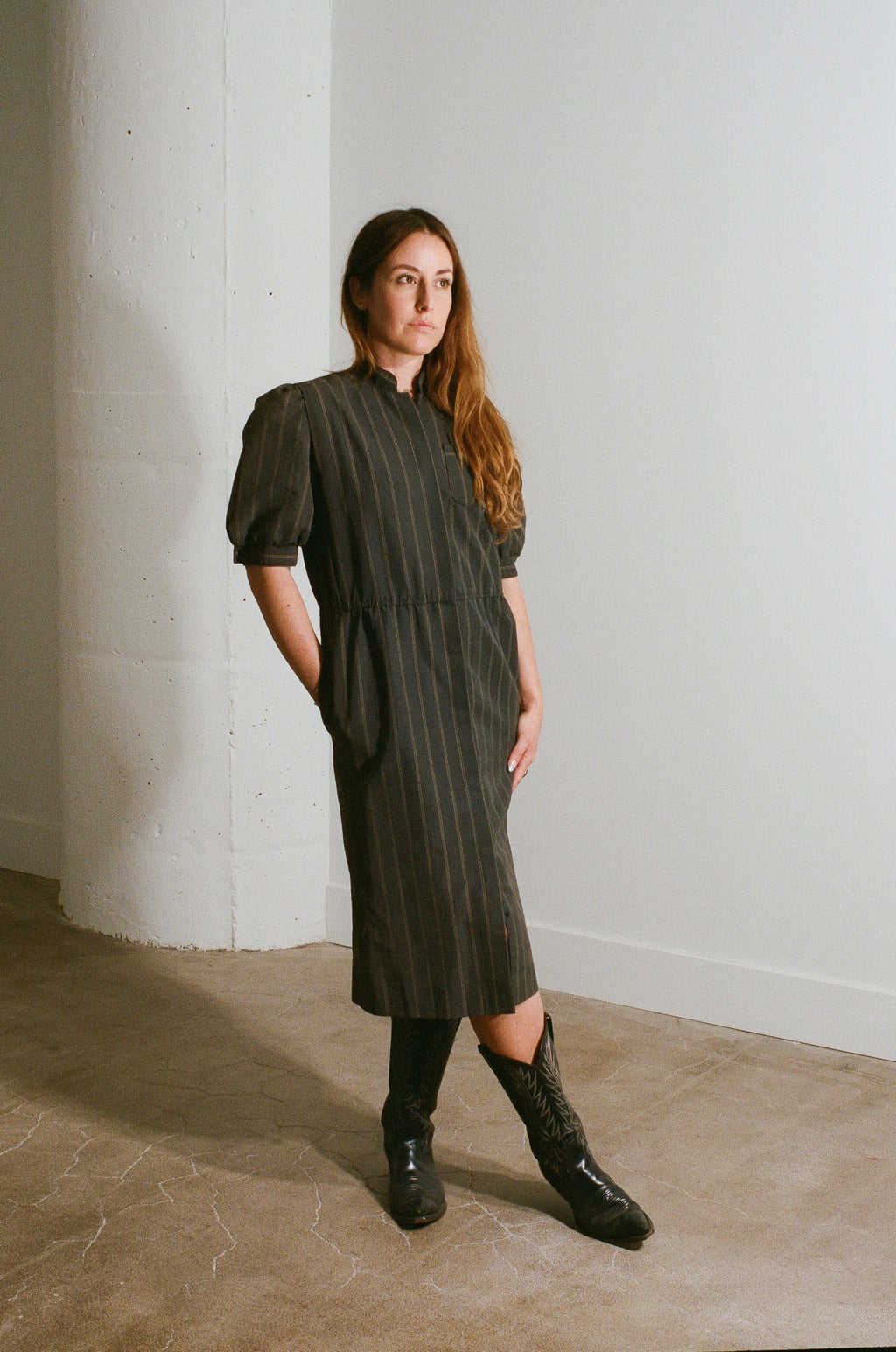 Woman wearing a green dress standing against a white wall.