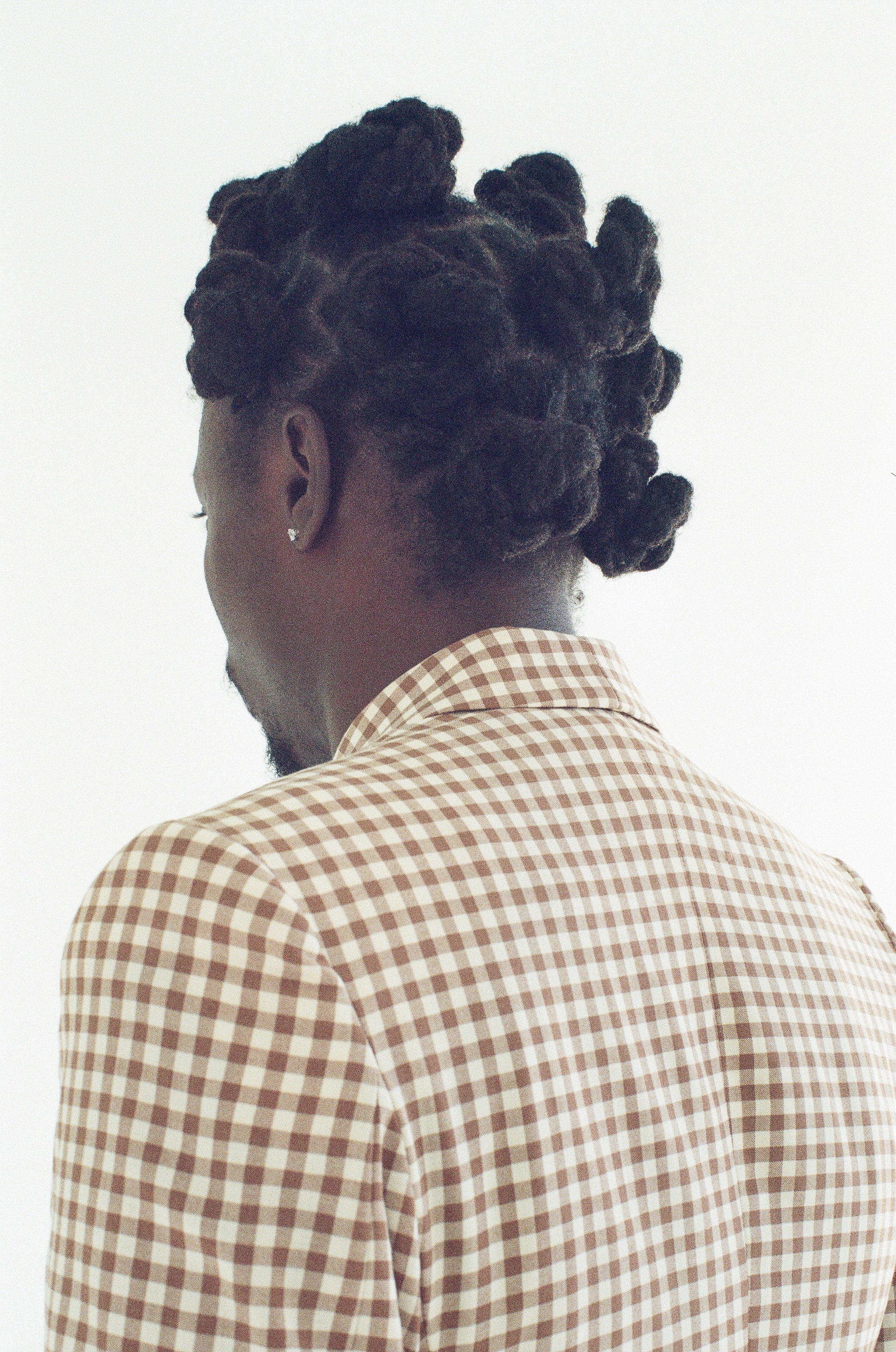 Person wearing a checkered shirt with braided hair on a white background