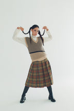 Woman wearing a patterned vest and plaid skirt on a white background