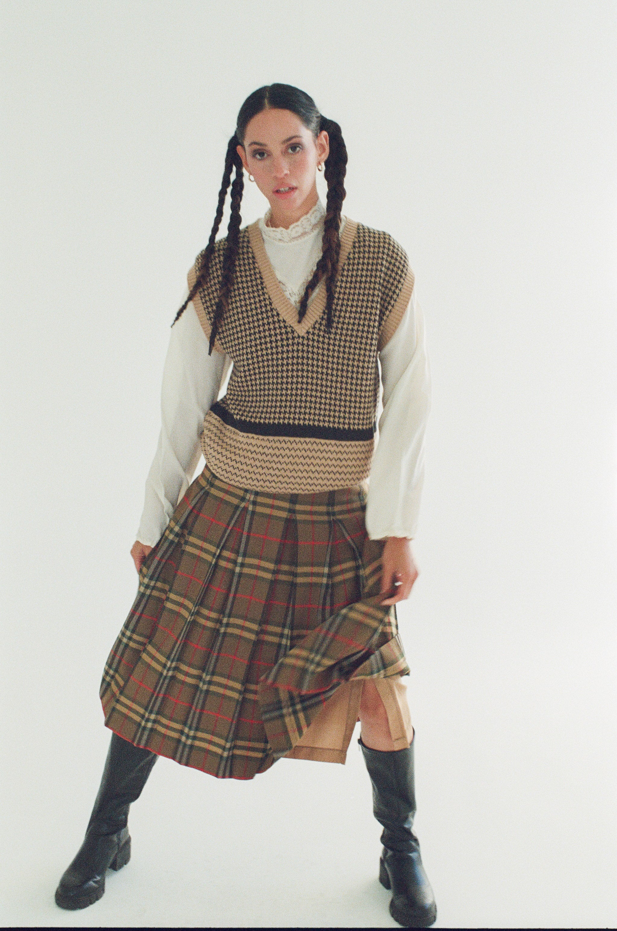 Person wearing a plaid skirt, checkered vest, and white turtleneck on a white background