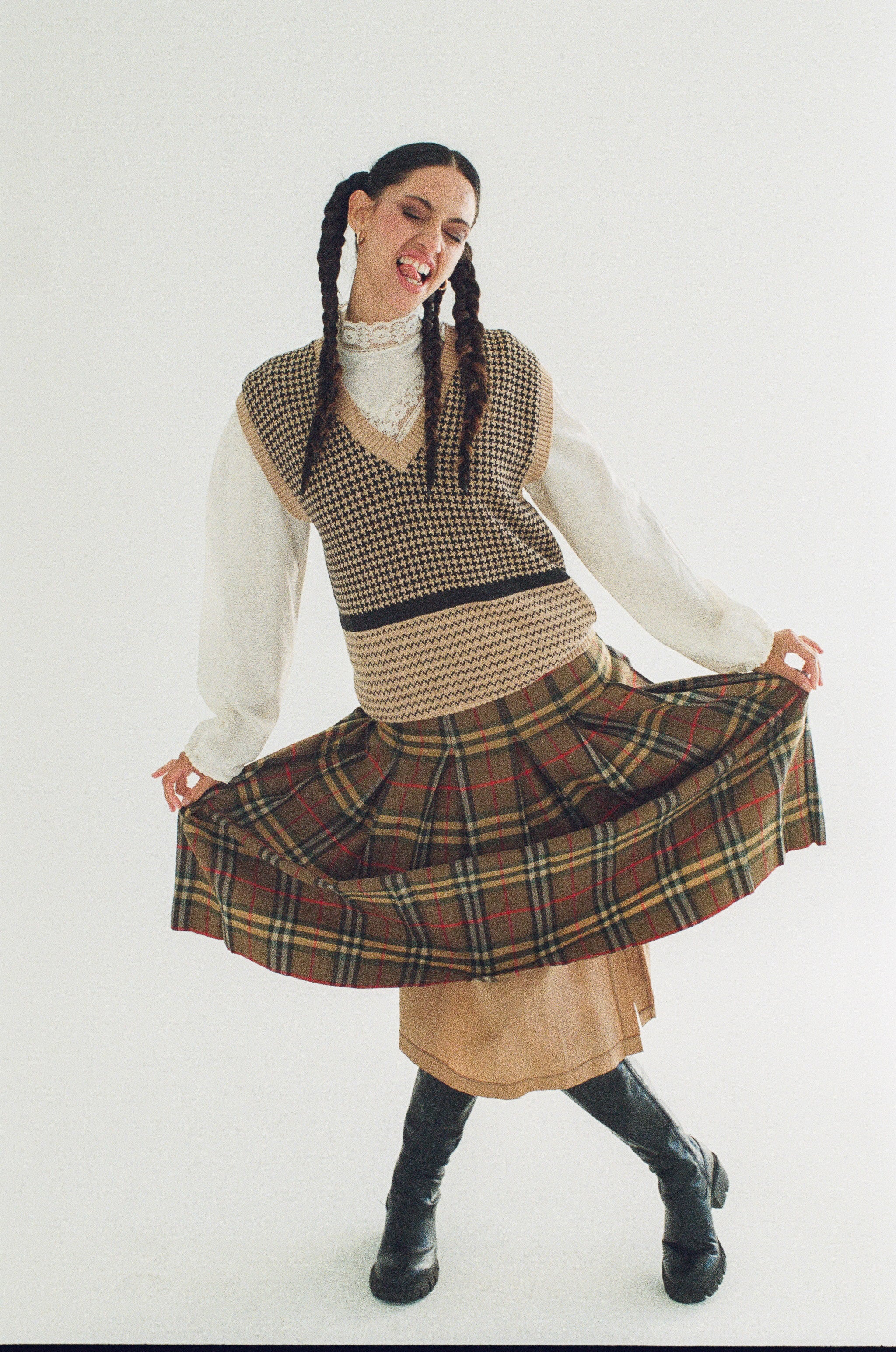 Person wearing a plaid skirt and checkered vest on a white background