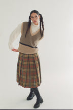 Woman wearing a patterned vest and plaid skirt on a white background
