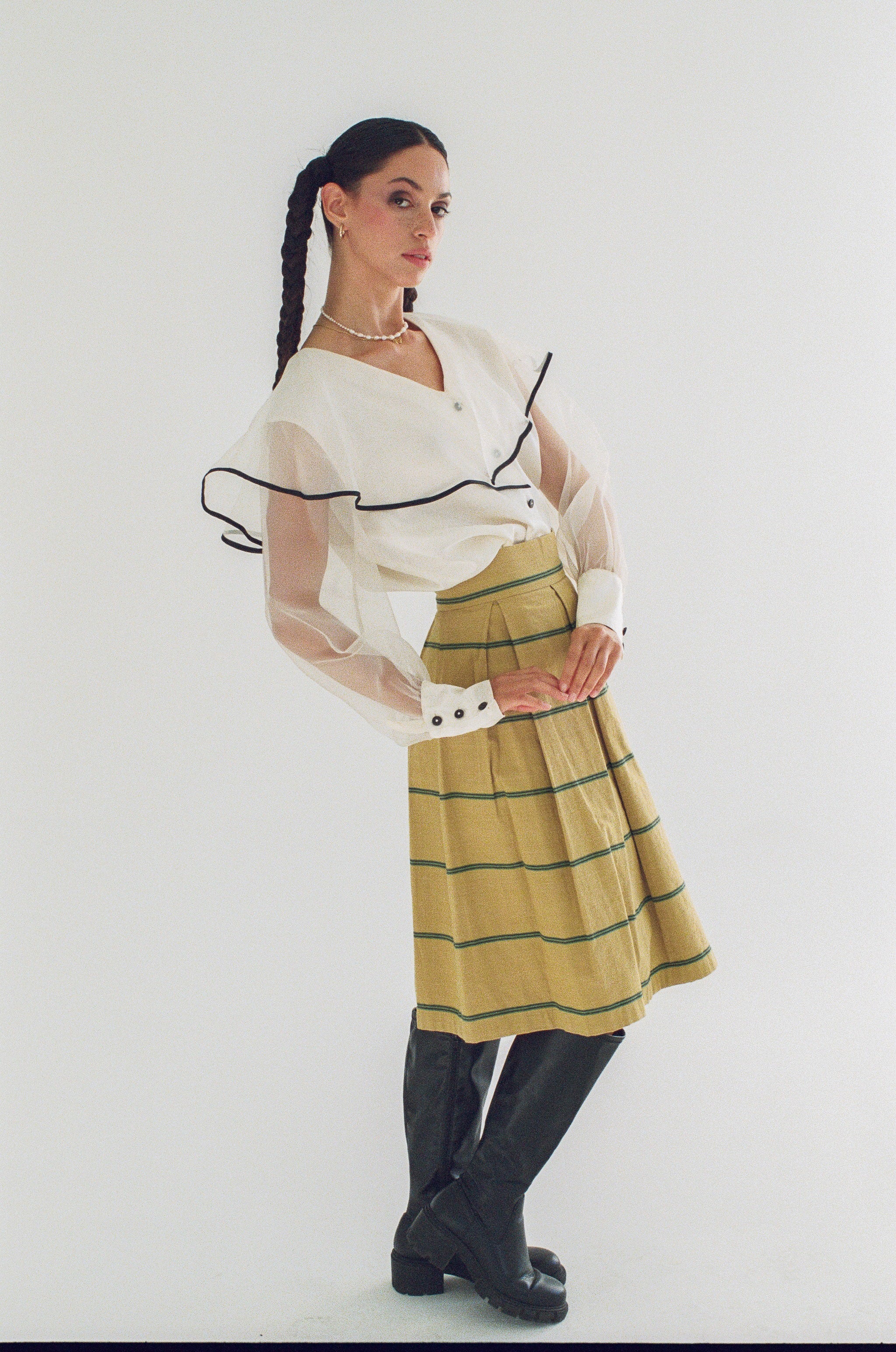Woman wearing a white blouse with black accents and a yellow plaid skirt on a white background