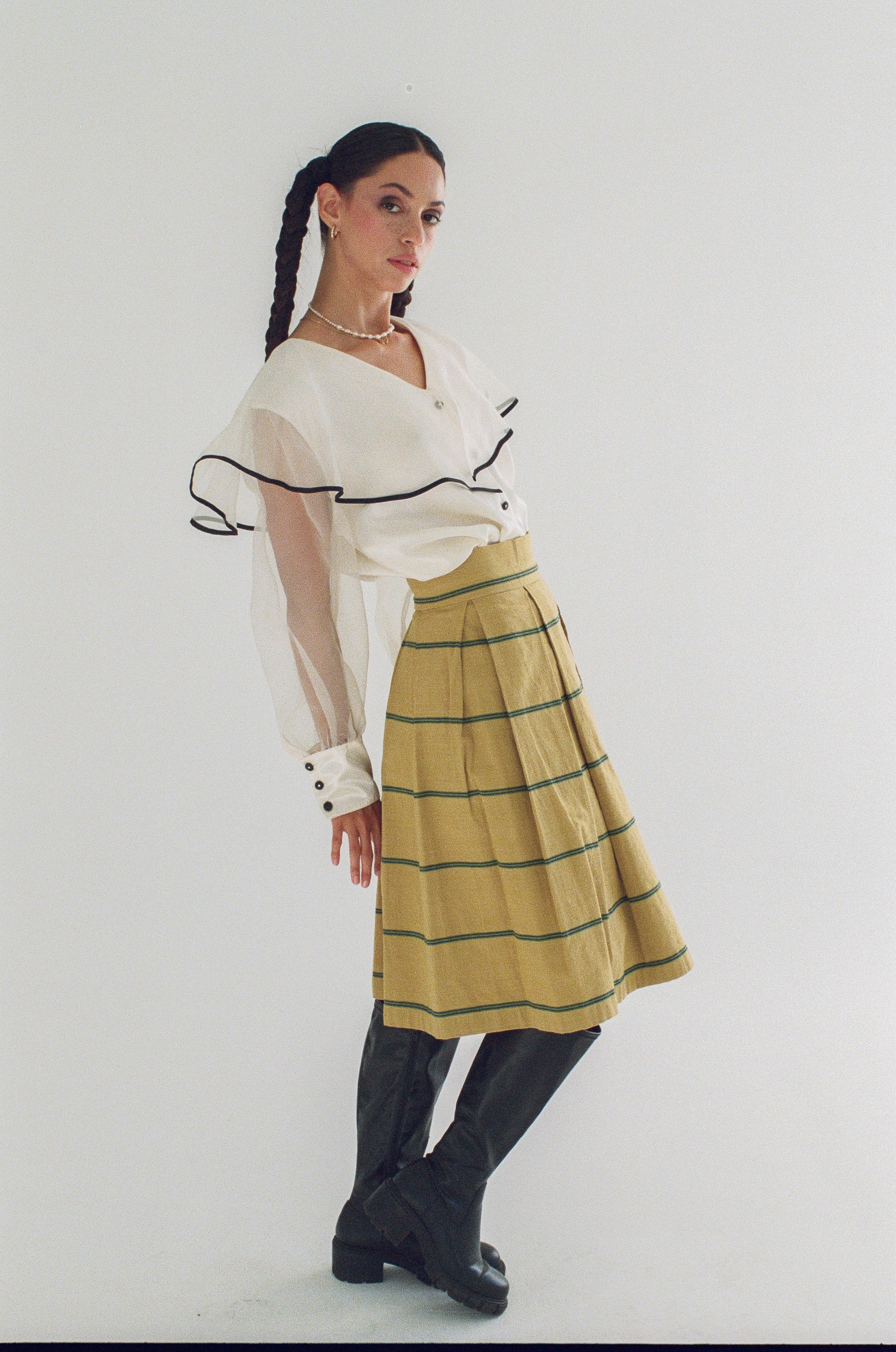 Woman wearing a white blouse with black trim and a yellow plaid skirt on a white background