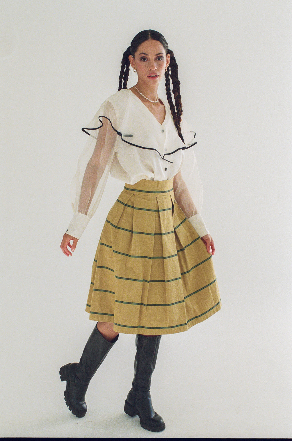 Woman wearing a white blouse with black trim and a yellow plaid skirt on a white background
