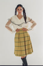 Woman wearing a white blouse with black trim and a yellow plaid skirt on a white background