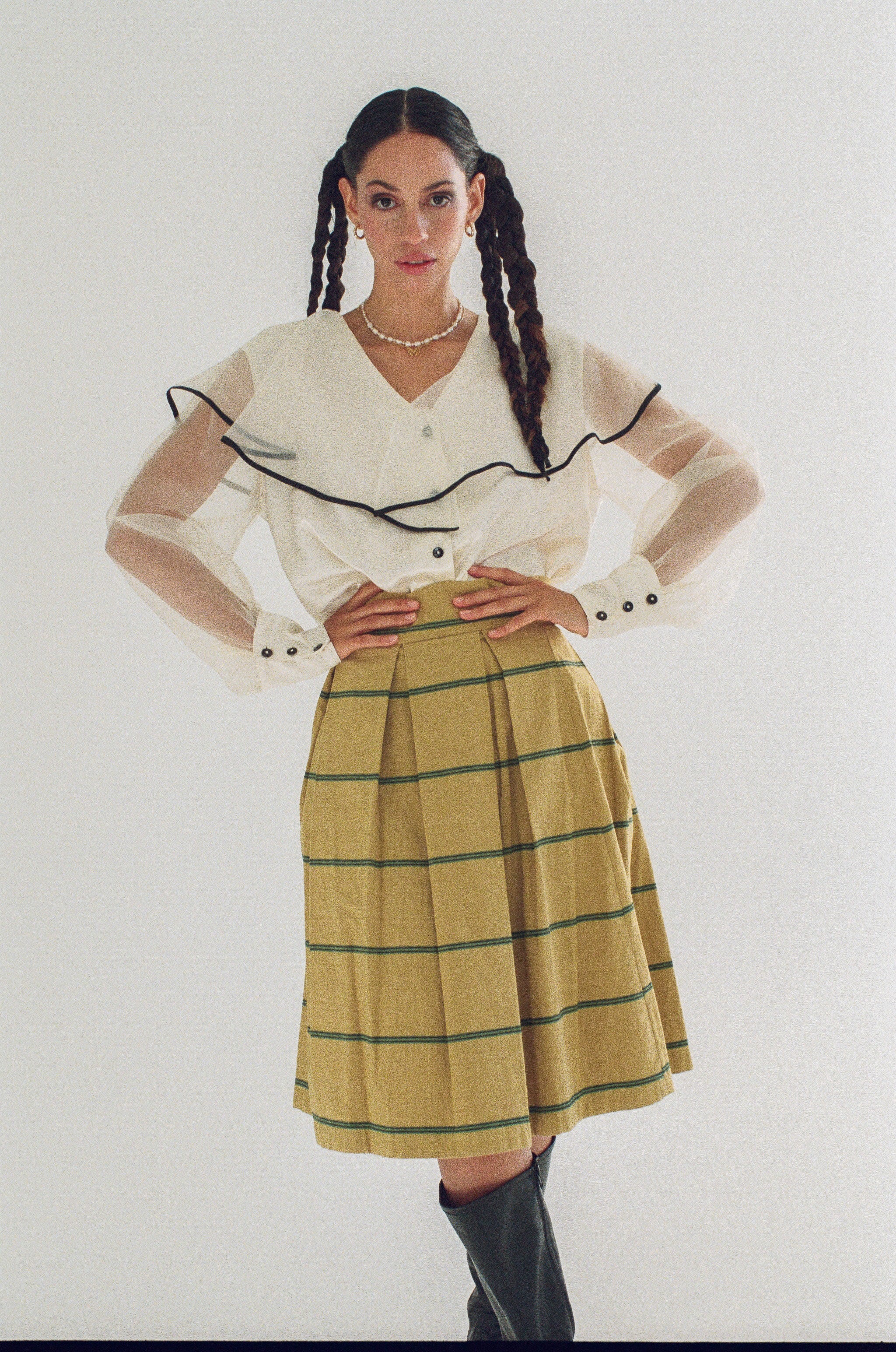 Woman wearing a white blouse with black trim and a yellow plaid skirt on a white background