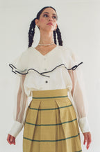 Woman wearing a white blouse with black accents and a yellow striped skirt on a plain background