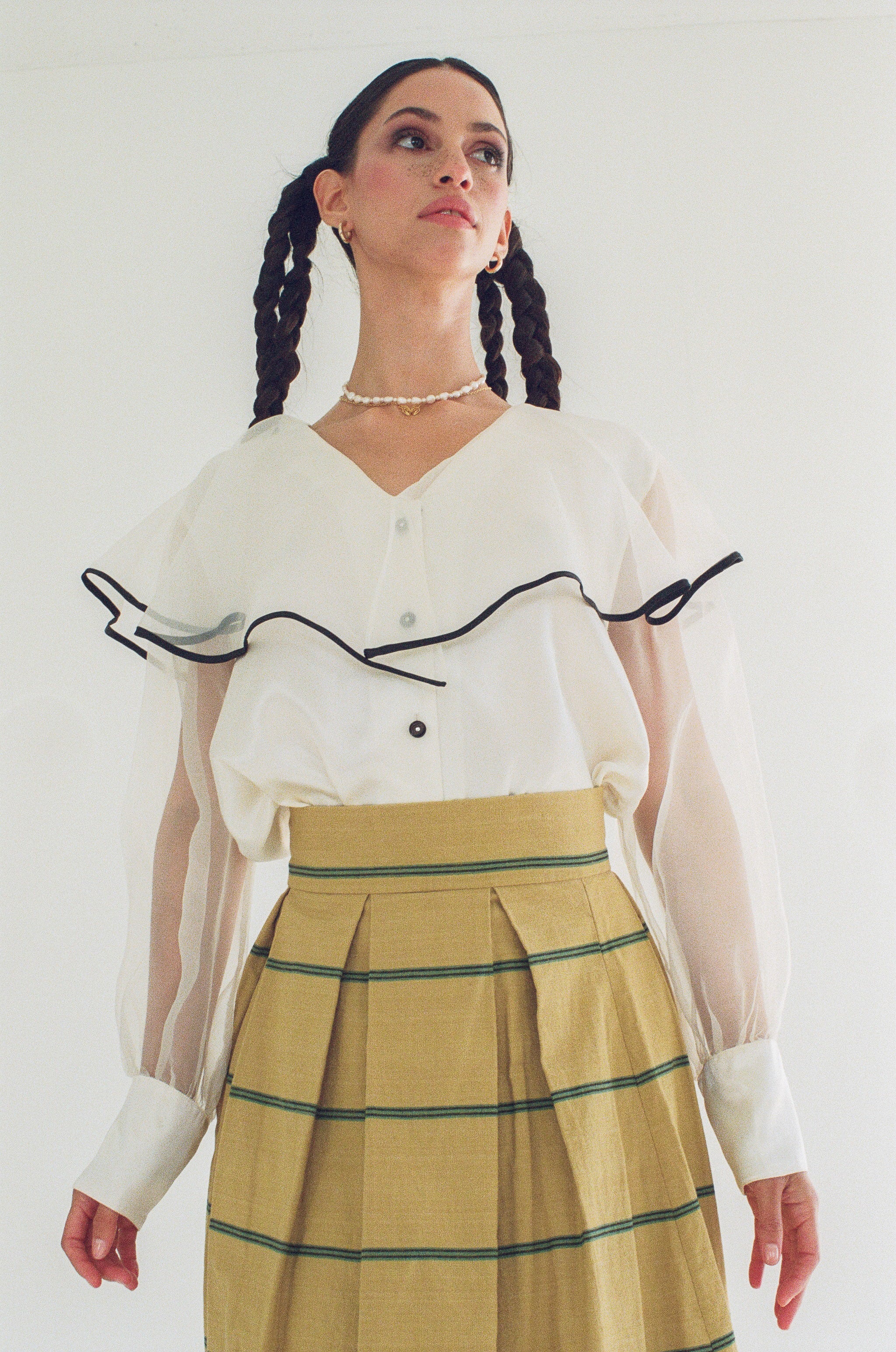 Woman wearing a white blouse with black accents and a yellow striped skirt on a plain background