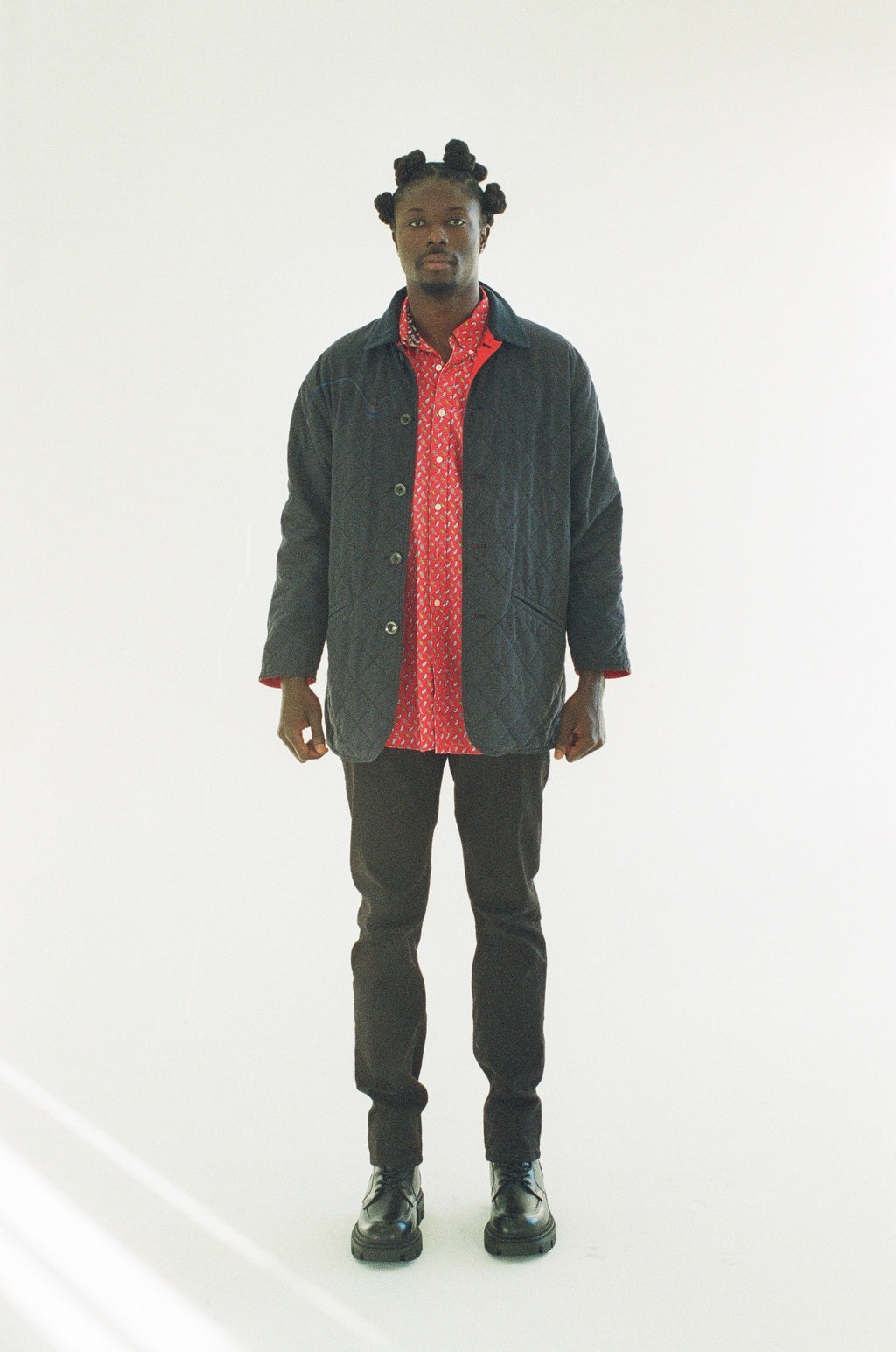 Man wearing a black jacket over a red shirt with black pants on a white background