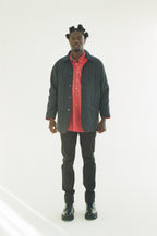 Man wearing a black jacket over a red shirt with black pants on a white background