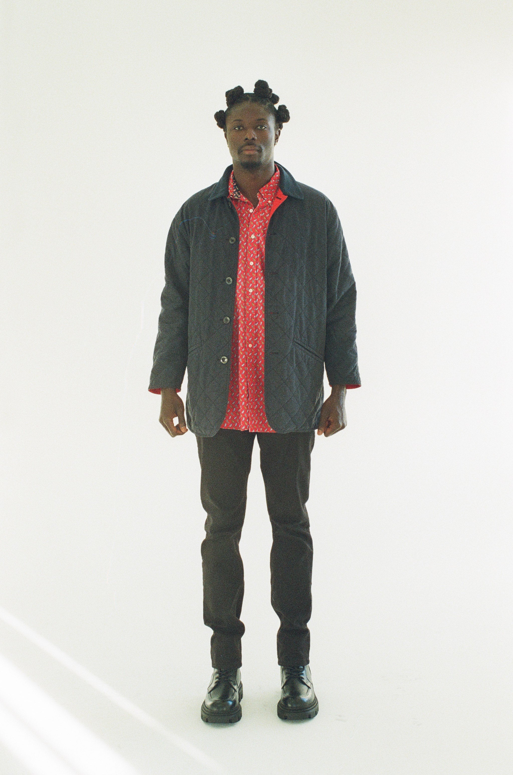 Man wearing a black jacket over a red shirt with black pants on a white background