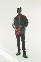 Man wearing a black jacket over a red shirt with black pants on a white background