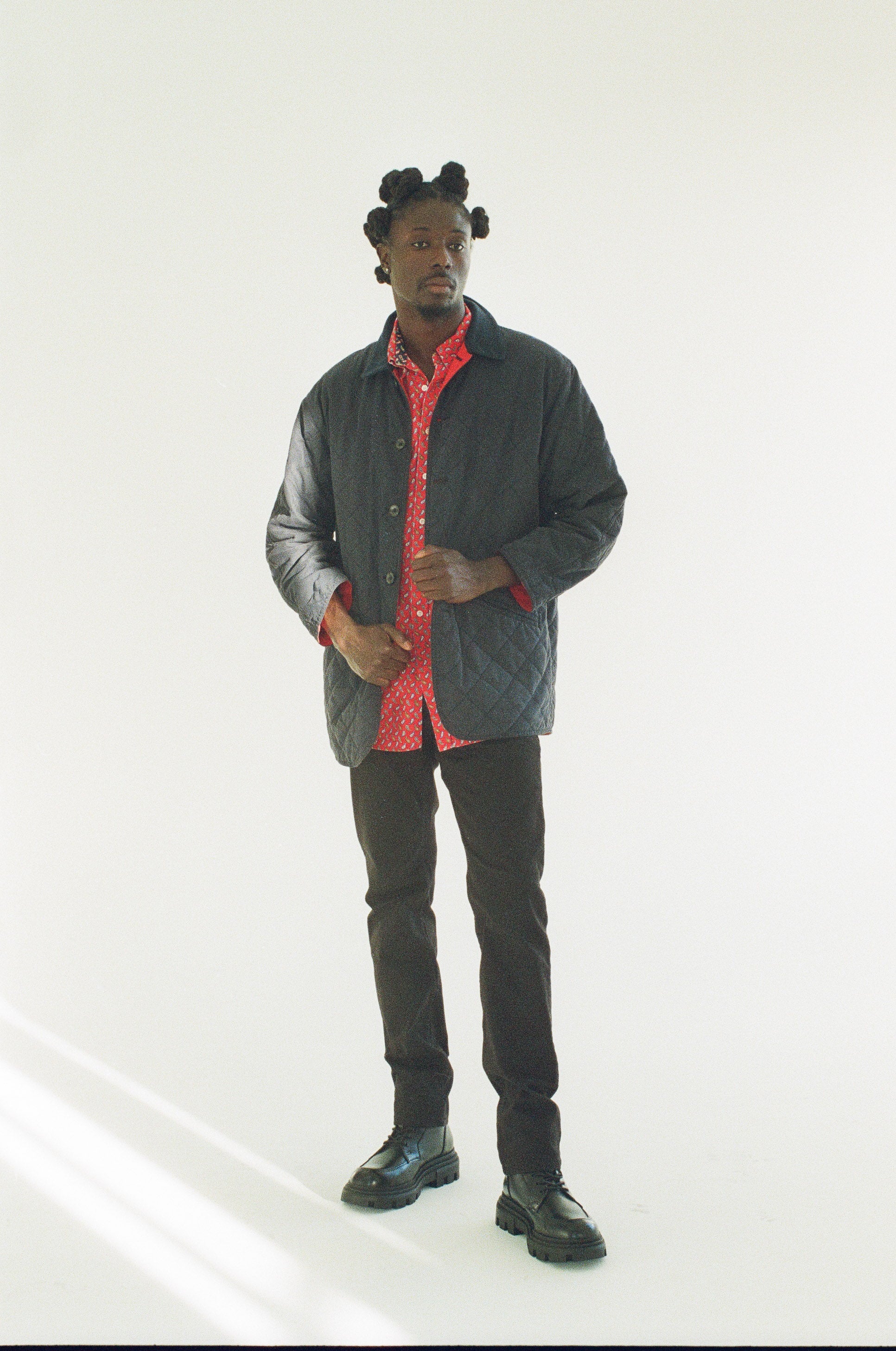 Man wearing a black jacket over a red shirt with black pants on a white background