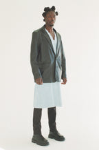 Person wearing a black blazer over a white dress on a white background